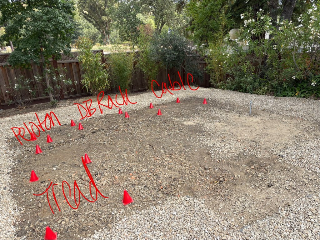 Backyard gravel area with red spray-painted markings and cones laying out planned gym equipment positions labeled Peloton, DB Rack, Cable, and Tread