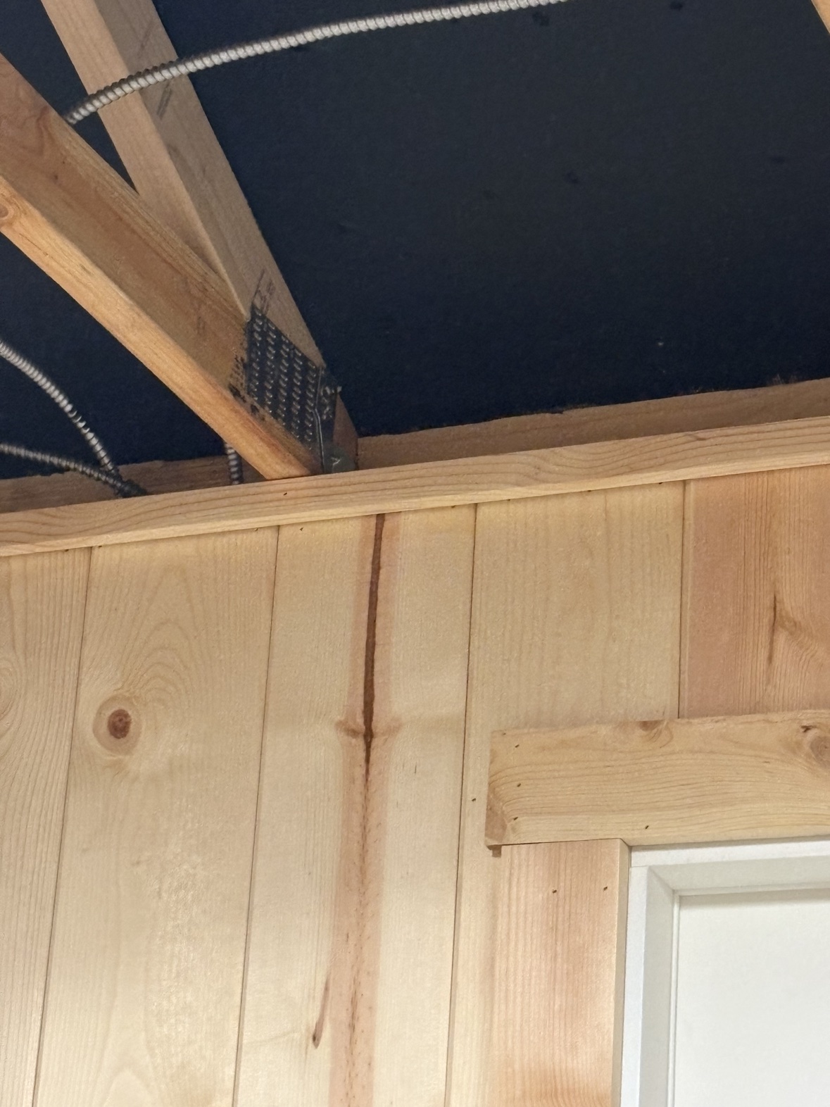 Pine plank wall meeting the ceiling with wood trim below the open rafters