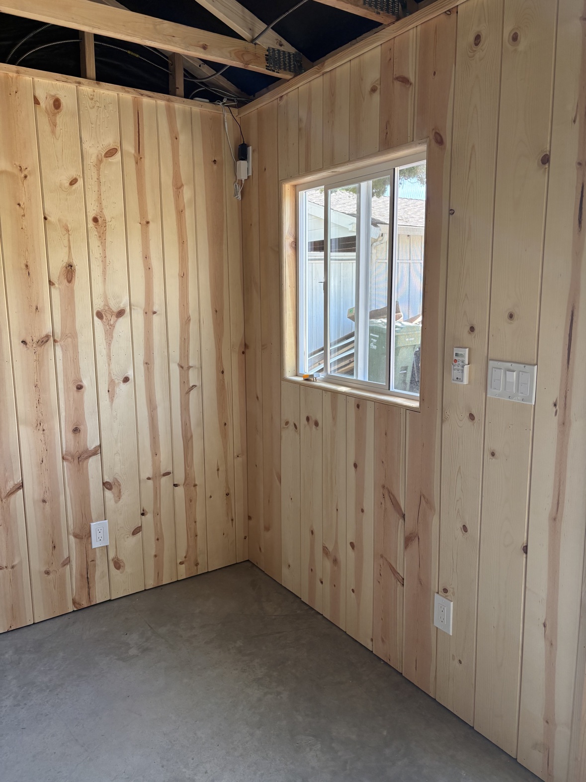 Finished rustic pine plank walls in the shed gym with a window, outlets, and concrete floor