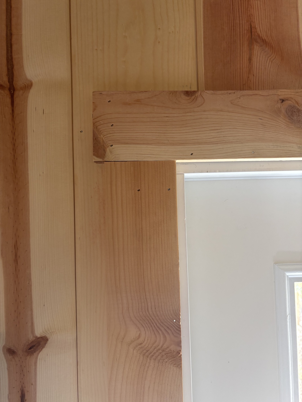 Close-up of wood casing trim around a door meeting the pine plank wall