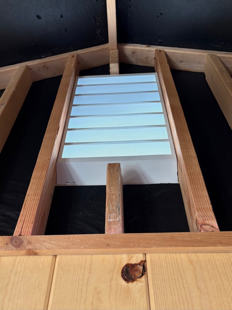 White gable vent installed between wooden framing inside the gym shed