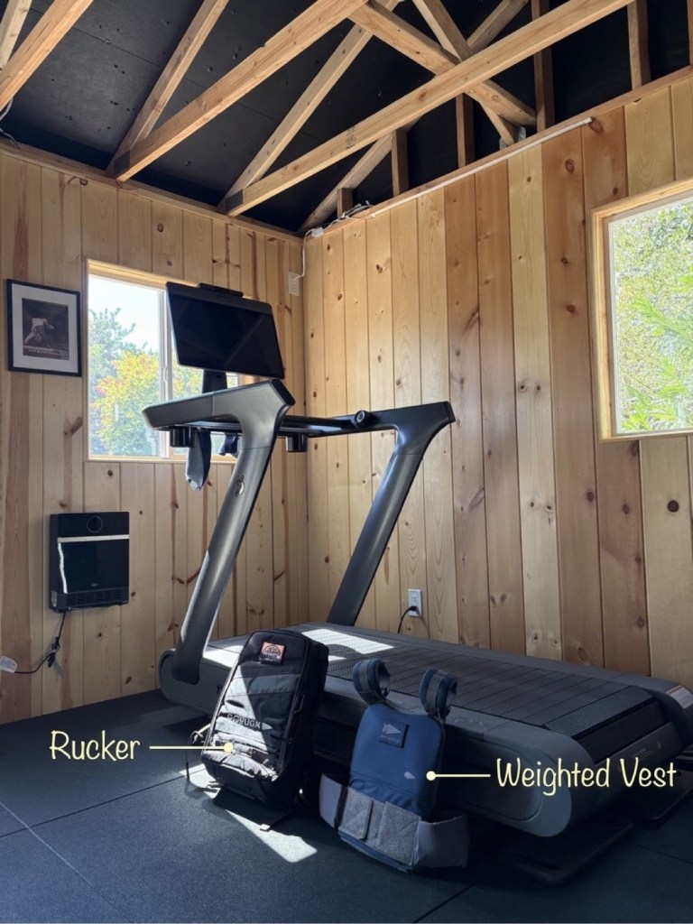 GORUCK Rucker backpack and weighted vest labeled next to the Peloton Tread+ in the shed gym